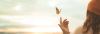 Einladung Taufe Text: Ausschnitt einer Person mit Mütze von hinten, sie streckt den Zeigefinger in die Luft und ein Schmetterling fliegt auf ihn zu, strahlender Himmel im Hintergrund