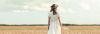 Einladung Taufe Text: Frau von hinten in weißem Kleid auf einem Feld, blauer Himmel