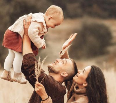 Fürbitten Taufe: kleine Familie auf einem Feld, Kind wird glücklich hochgehoben, sie schauen sich grinsend an